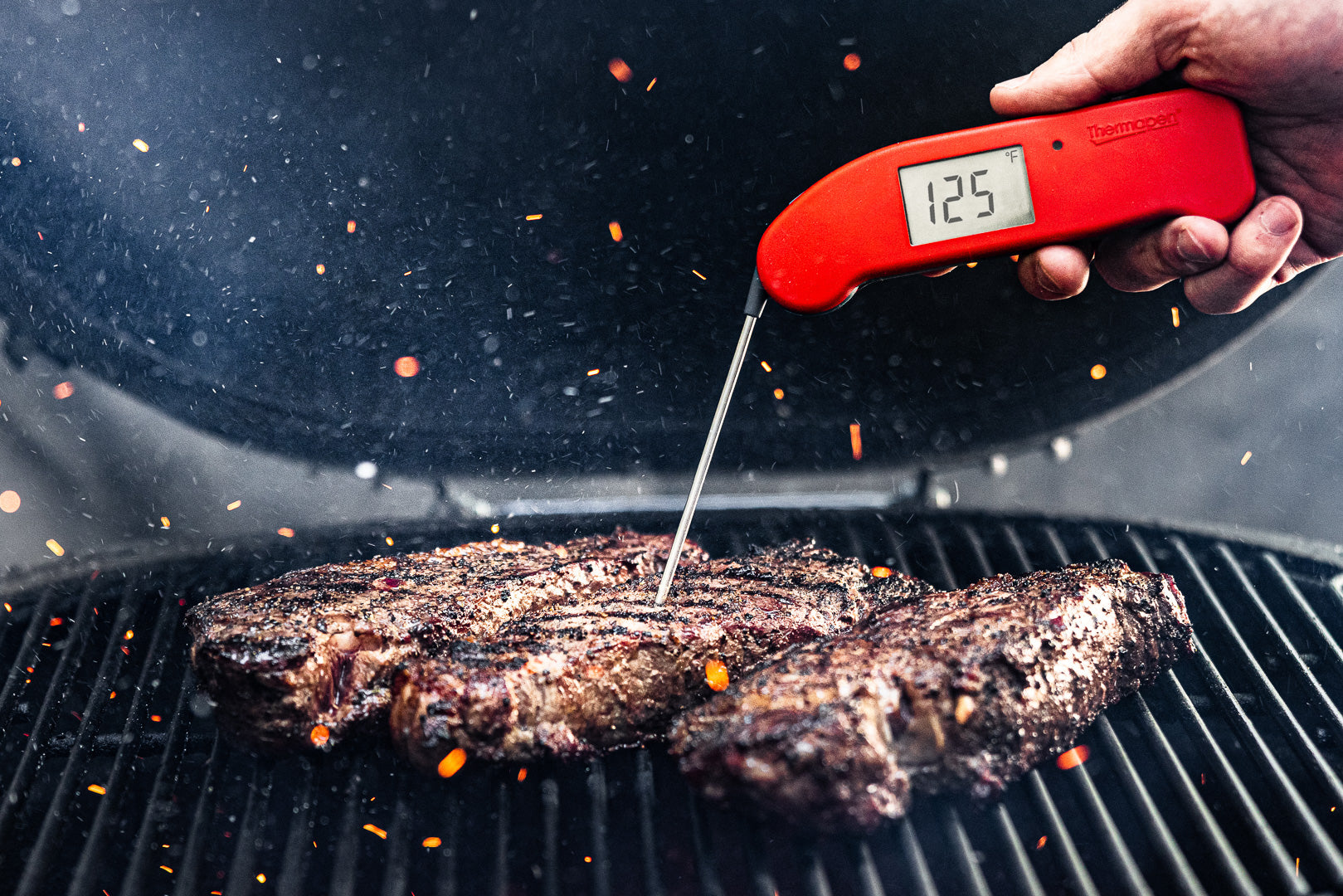 person using thermoworks thermometer in a steak on the grill