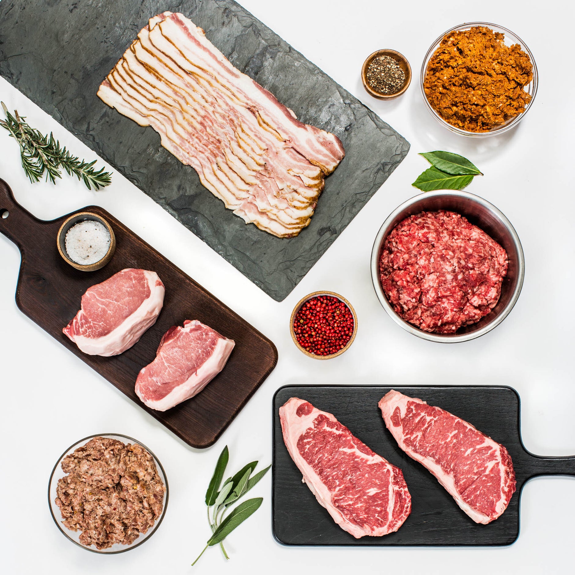Assorted Porter Road meats including steaks, bacon, pork chops, and ground beef with herbs and seasonings