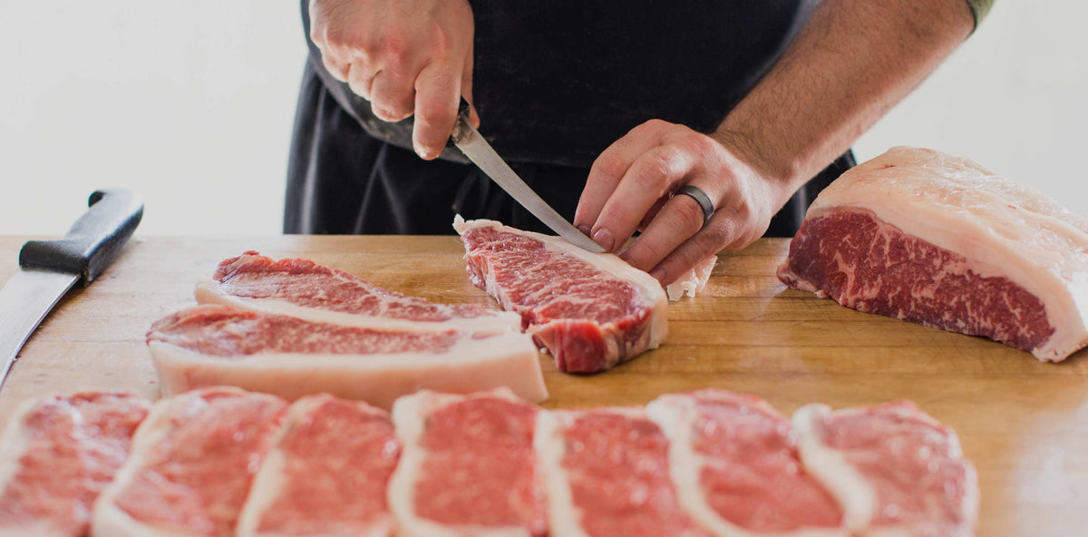Porter Road butcher trimming dry-aged steaks on a butcher block